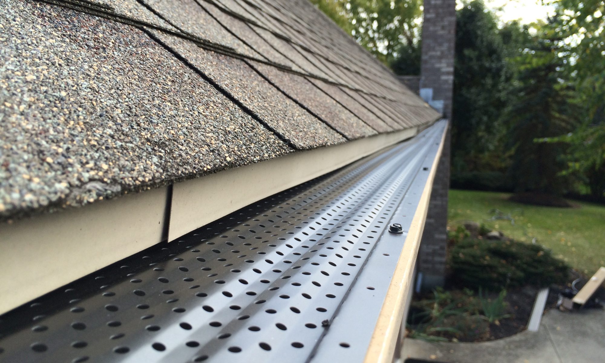Gutter guard installed beneath residential roof shingles